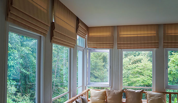An interior view of a bright corner sunroom featuring beige fabric Roman shades