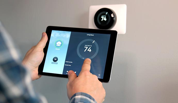 Person adjusting a smart thermostat using a tablet displaying temperature settings for the living room
