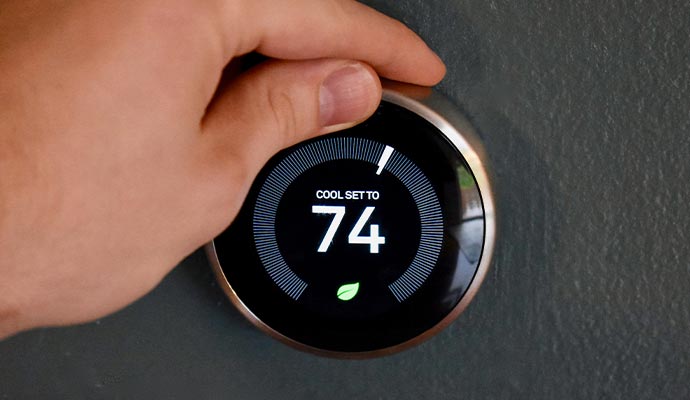 Person adjusting a smart thermostat mounted on a wall