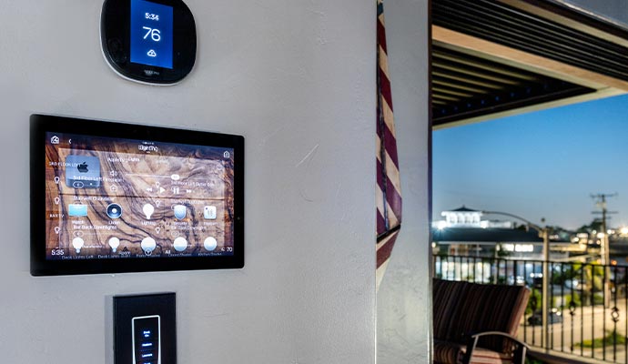 Smart home control panel and thermostat mounted on a wall near a balcony with city view