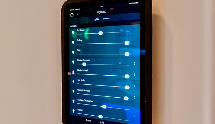Smart home control panel mounted on a wall showing adjustable lighting settings for multiple rooms